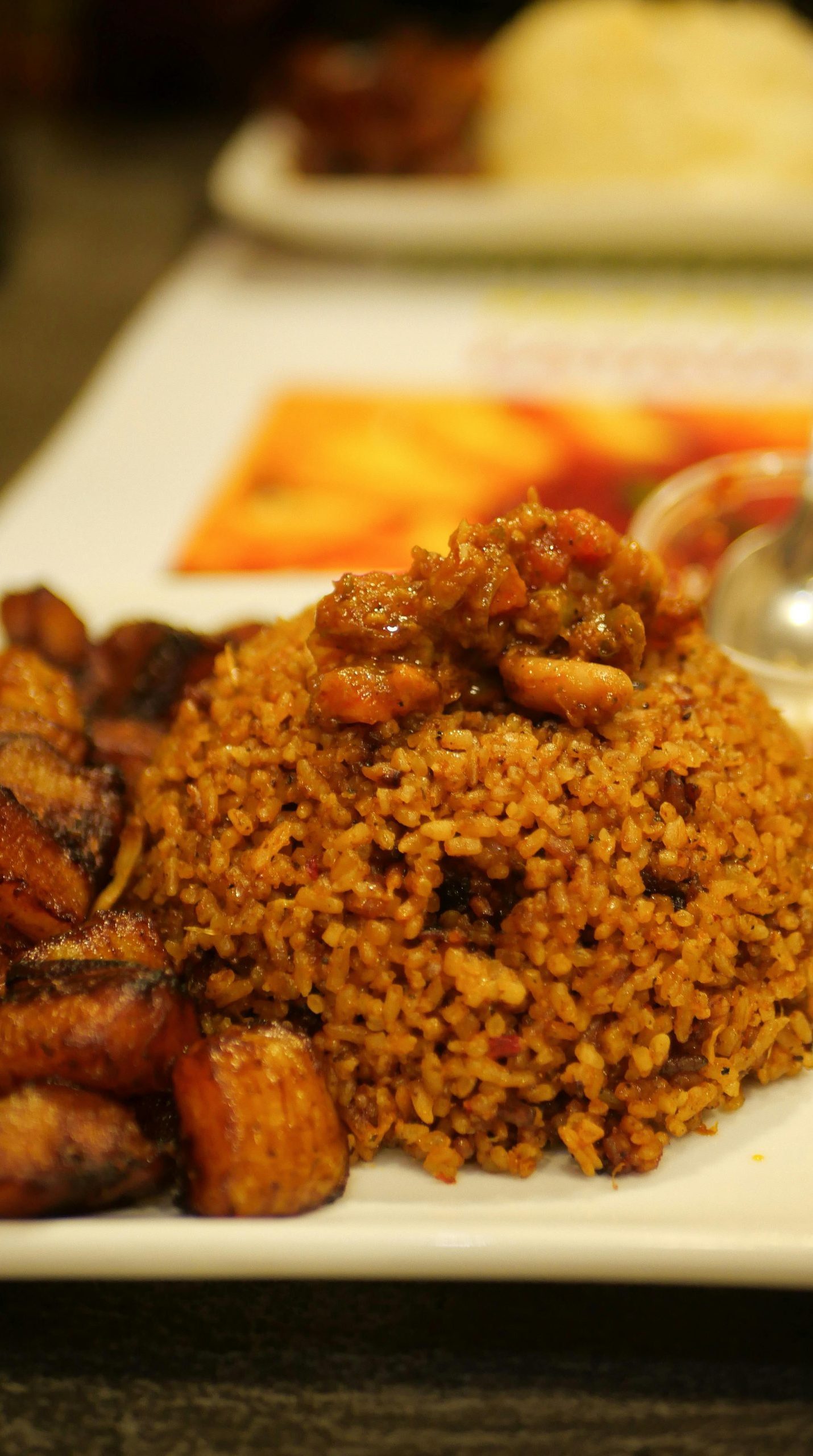 A tempting plate of Jollof rice accompanied by savory fried plantains. Perfect meal idea.